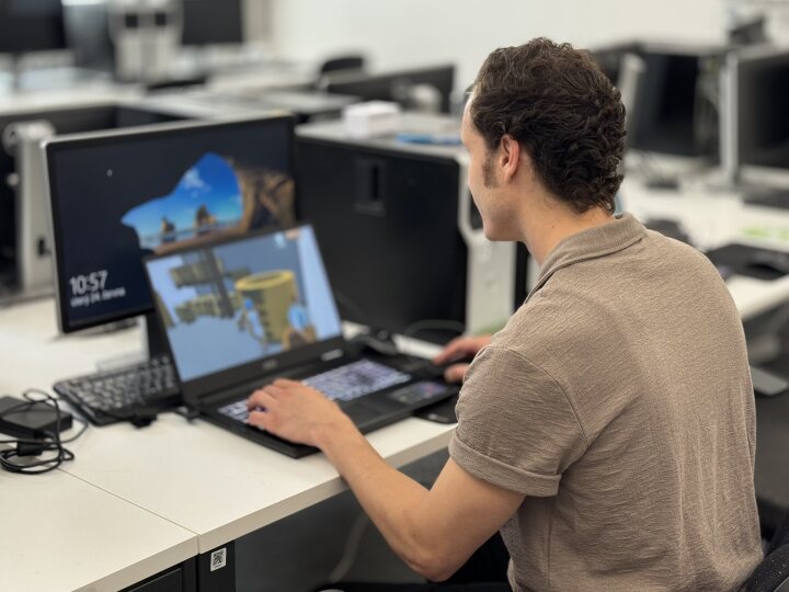 A man sitting at a desk in a modern computer room, working on a laptop.